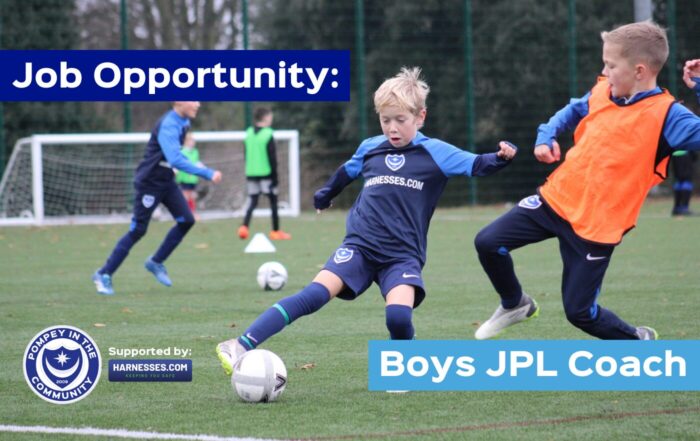 Boys playing football on grass wearing blue Pompey in the Community kit and an orange bib.