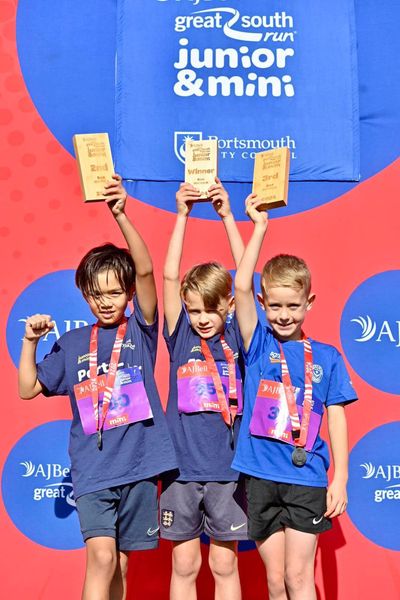 Three young runners standing on the Great South Run podium holding their trophies for coming in the top 3